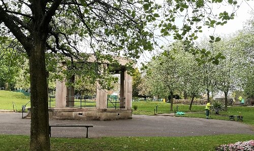 A park with grass, a tree and a stone bandstand