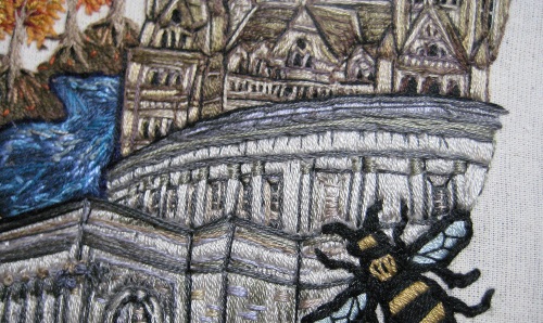 embroidery of a bee flying over a town
