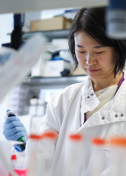 Female scientist in lab setting wearing lab coat and blue latex gloves.
