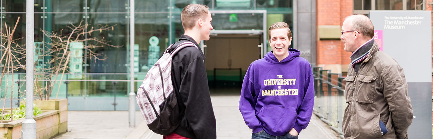 Male Manchester student ambassador greeting a father and son.