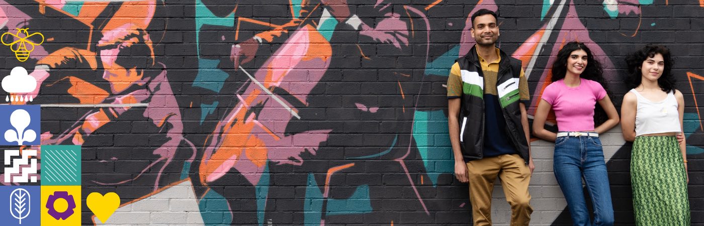 Three students stand against a graffitied wall.