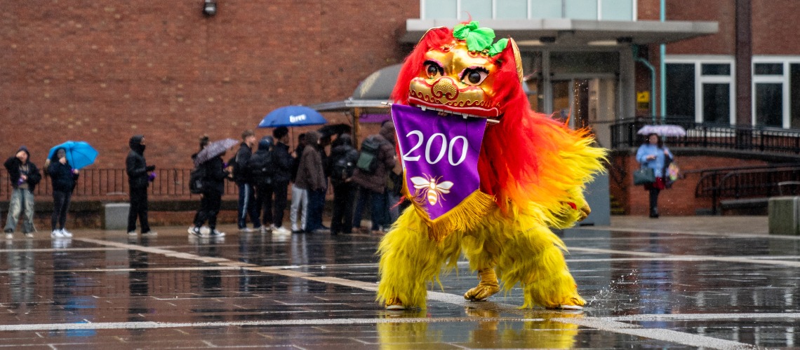 A human-operated lion performs a Lion Dance with a bicentenary banner in its mouth.