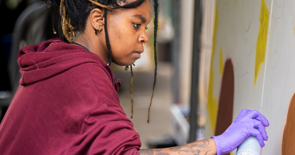 A woman spray paints as part of the Art of Research event.