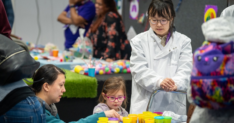 A child is instructed by a scientist at a Community Fair stall.