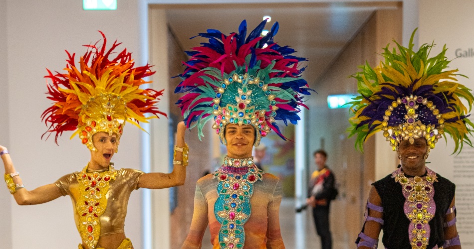 Three men in colourful carnival dress at the Whitworth.