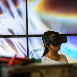 A woman uses a VR headset in front of a digital screen.