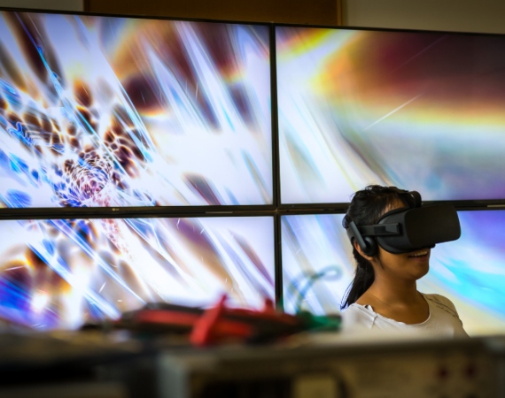 A woman uses a VR headset in front of a digital screen.