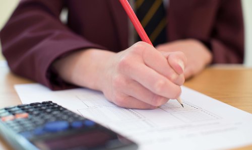 Student writing with a pencil and calculator is in the foreground