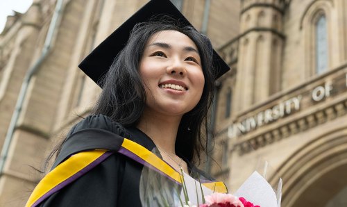 An Alumnae stood underneath the iconic University of Manchester sign.