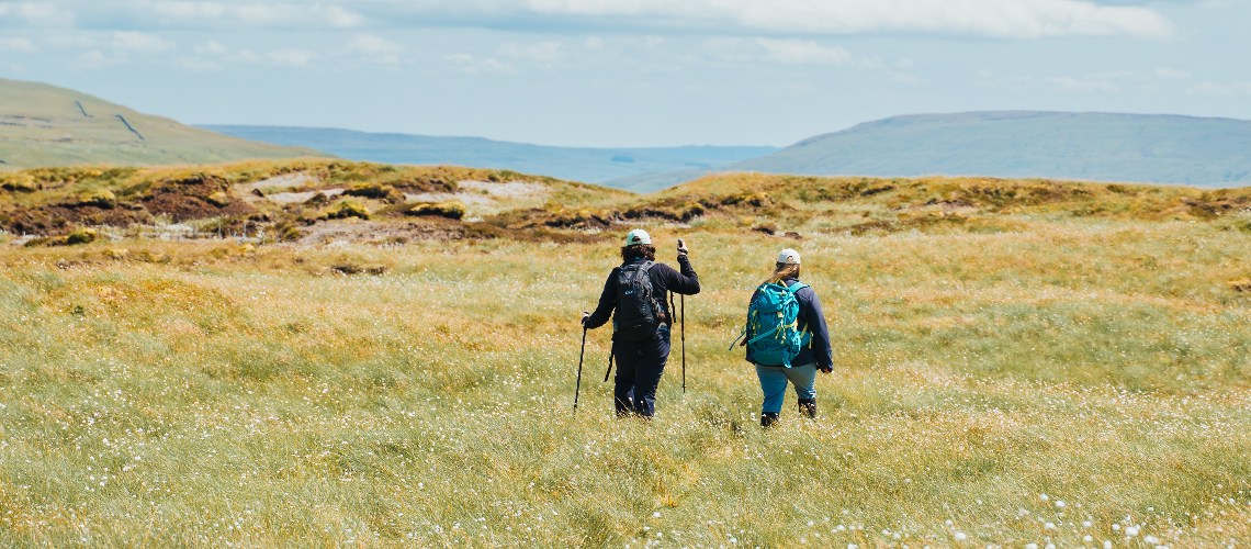 People walking across open moorland landscape.