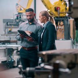 Man and woman validating information on an iPad against the back drop of a factory