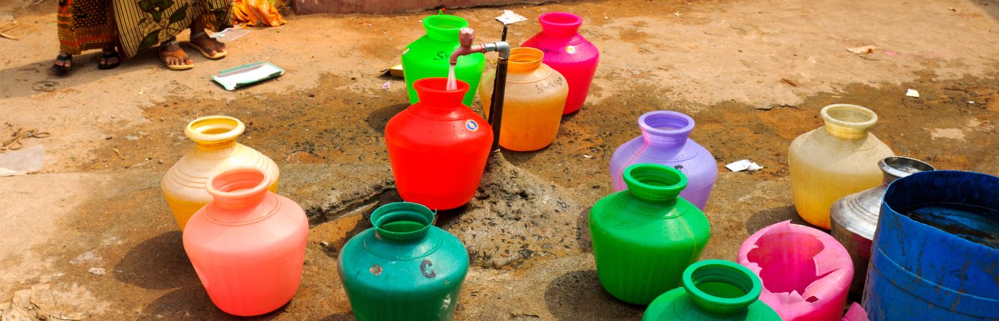 A number of colourful buckets next to a tap.