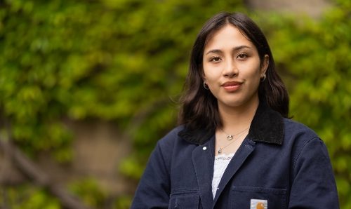 Student smiling stood against the Beyer Building, The University of Manchester 