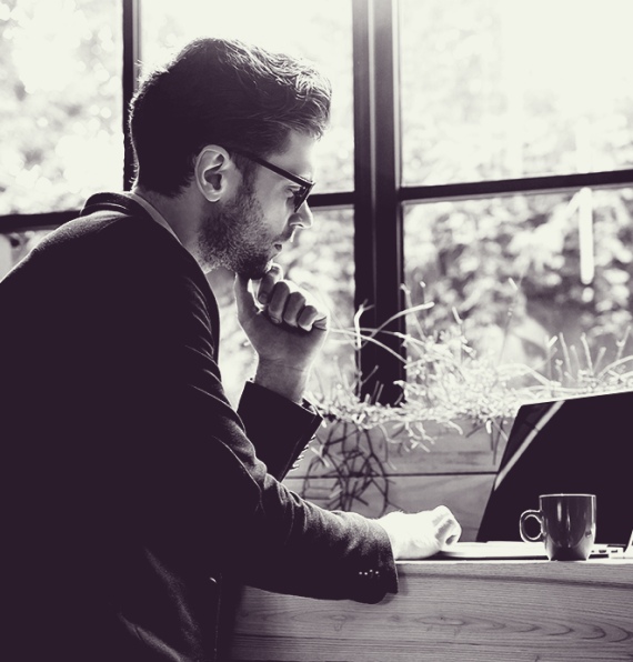 Black-and-white image of a man in glasses working on a laptop.