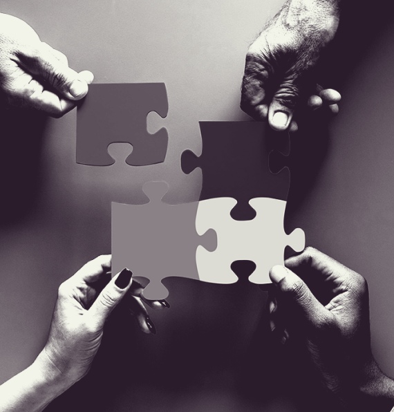Black-and-white image of four hands connecting a jigsaw puzzle.