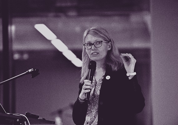 Black-and-white image of a woman speaking into a microphone and gesturing with her hand