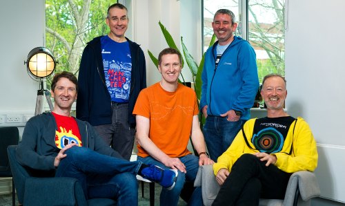 Five men sitting together and smiling, wearing casual University of Manchester branded clothing
