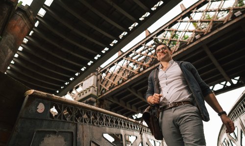 Man in business attire walking and looking up at an old railway bridge structure
