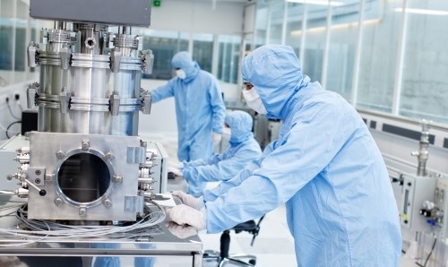 Two researchers in blue cleanroom suits and masks working with laboratory equipment