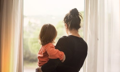 A parent holding their child while looking out of a window.
