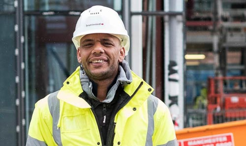A man in a hard hat and a high vis smiles at the camera