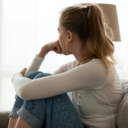 Young person with ponytail sitting on sofa looking out window