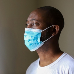 A young black man wearing a blue facemask. Image (c) iStock.