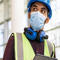 A construction worker wearing full safety gear, including a hard hat and mask. 