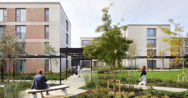 Students sit around and stroll through a green and spacious part of their accommodation complex.