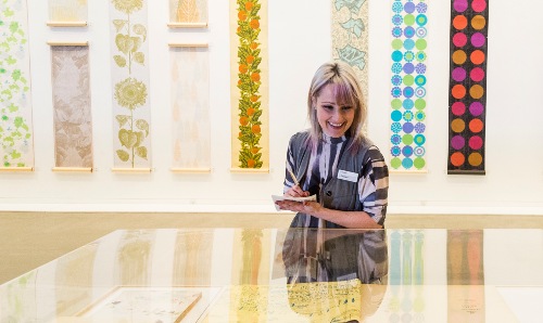 A woman smiling while looking at a display in Whitworth Art Gallery.