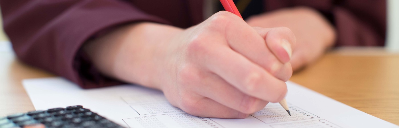 Student in burgundy school uniform sitting down and writing using a pencil and paper with a calculator in the foreground