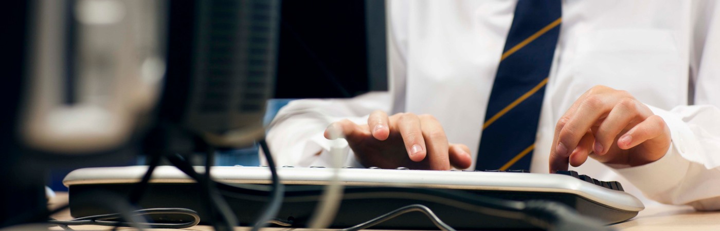 Student in a white shirt and blue striped tie using a desktop computer