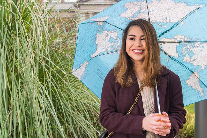 A student smiling and holding an umbrella with a map of the world design. 