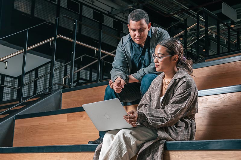 A teacher and a student sitting on stairs using a laptop.