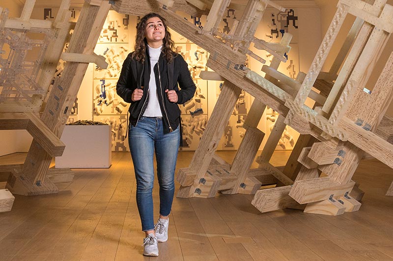 A student walks beneath a wooden sculpture at Whitworth Art Gallery.