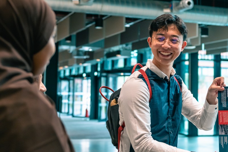 A student smiles widely while talking to a fellow student in Engineering Building A.