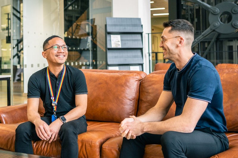 Two men chat and laugh while sitting on a sofa.