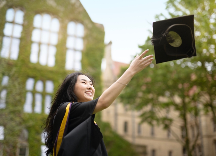 A women smiling as she throws her mortarboard into the air at graduation