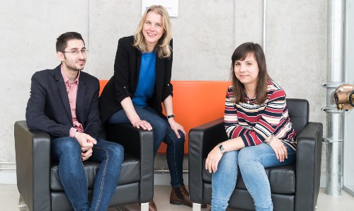 Two women and one man sitting on sofas looking at the camera