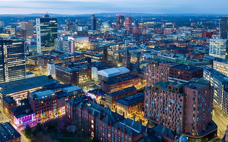 Cityscape of Manchester at dusk with lights glowing, symbolising innovation, growth, and urban life.