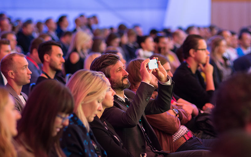 Audience at a conference listening to speakers, symbolising innovation, learning, and collaboration.