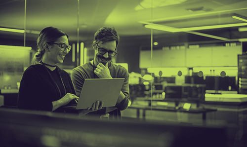 Two researchers smiling while reviewing work on a laptop, symbolising teamwork, research, and ideas.