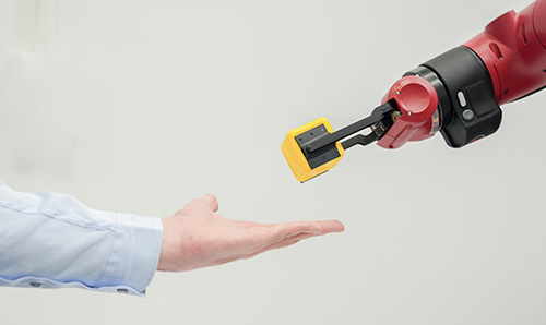 A robot arm passes a yellow block to a human hand.