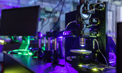 A microscope, bathed in purple light, with green laser accents.