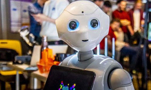 Humanoid robot with expressive eyes and tablet screen on chest, showcased at a technology event with people.