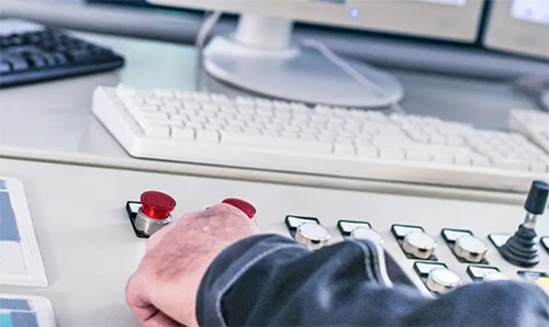 A hand at a control panel with red buttons.