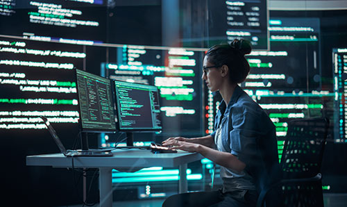Researcher working at multiple screens with code and data, symbolising computing and innovation.