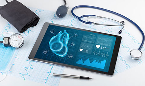 Tablet displaying heart health data alongside stethoscope, blood pressure monitor, pen, and medical charts.
