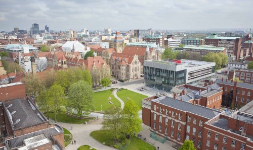 Aerial view of the University campus, showing Gilbert square, the Learning Commons beside grand old buildings. Manchester skyline in the background.