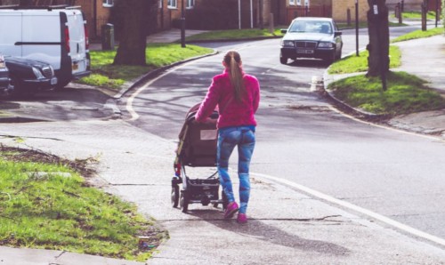 Woman walking pram down a street